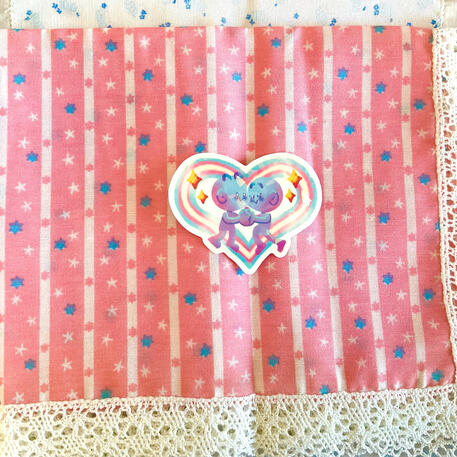 Foto de la pegatina trans for trans. A modo de decoración a su alrededor hay puesto un mantelito rosa con estrellas azules y blancas.