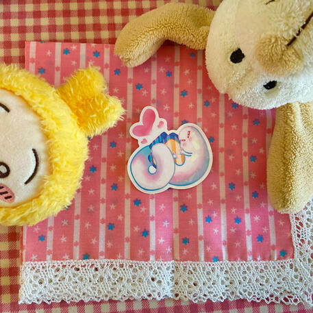 Foto de la pegatina de Brushbuddy (gusanito pincel) del manga Witch Hat Atelier. A modo de decoración a su alrededor hay: un peluche de un perro blanco y un peluche de Usagi de la serie Chiikawa.