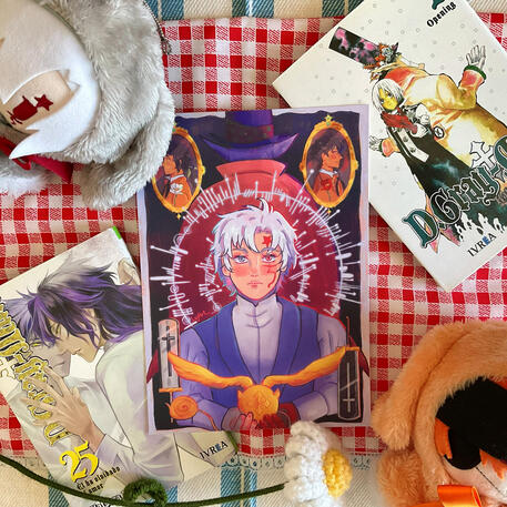 Foto de la print de D.Gray-man. A modo de decoración a su alrededor hay: el volumen 1 y 25 del manga, una flor de crochet y los peluches de Allen y Lavi.